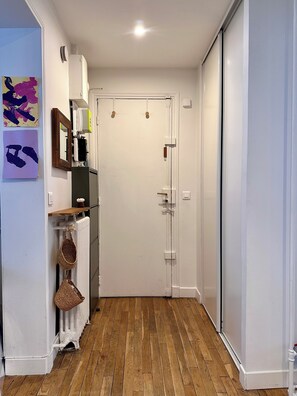 A narrow hallway with a wooden floor, a white radiator, a door with a handle, and a wall-mounted air conditioning unit. - Quiet & Bright • Line 1 • Direct access to the center (Paris)