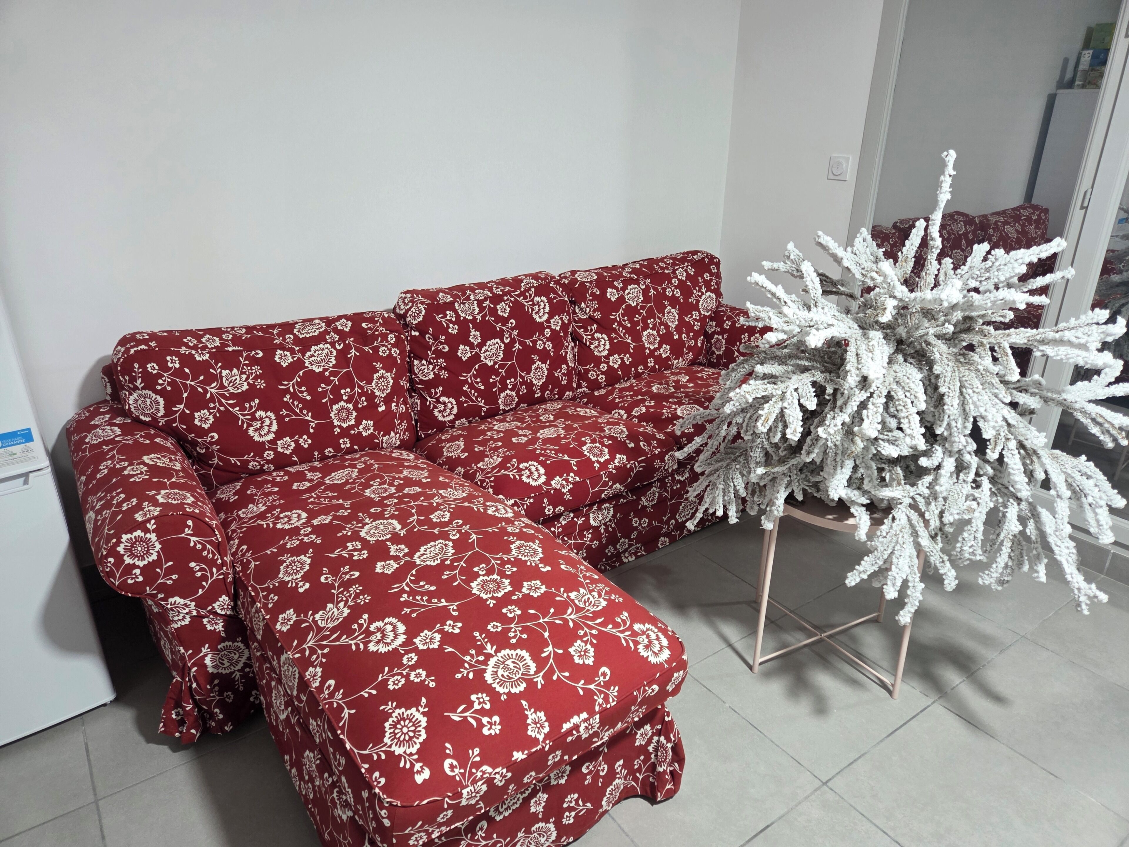 En röd soffa med blommönster i ett rum med en vit vägg och en vit prydnadsväxt.