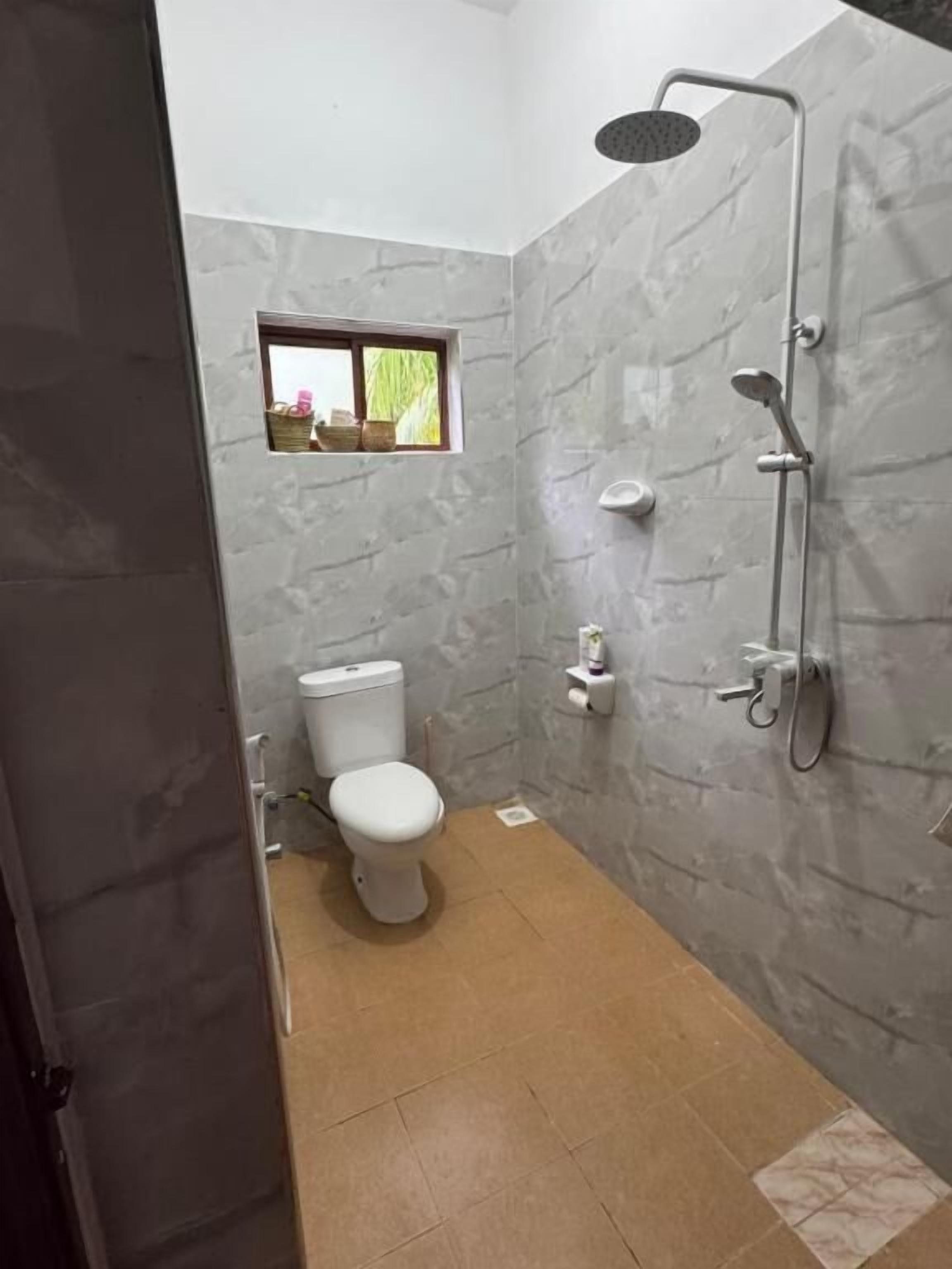 Un baño con inodoro, ducha y un pequeño ventanal con vistas.