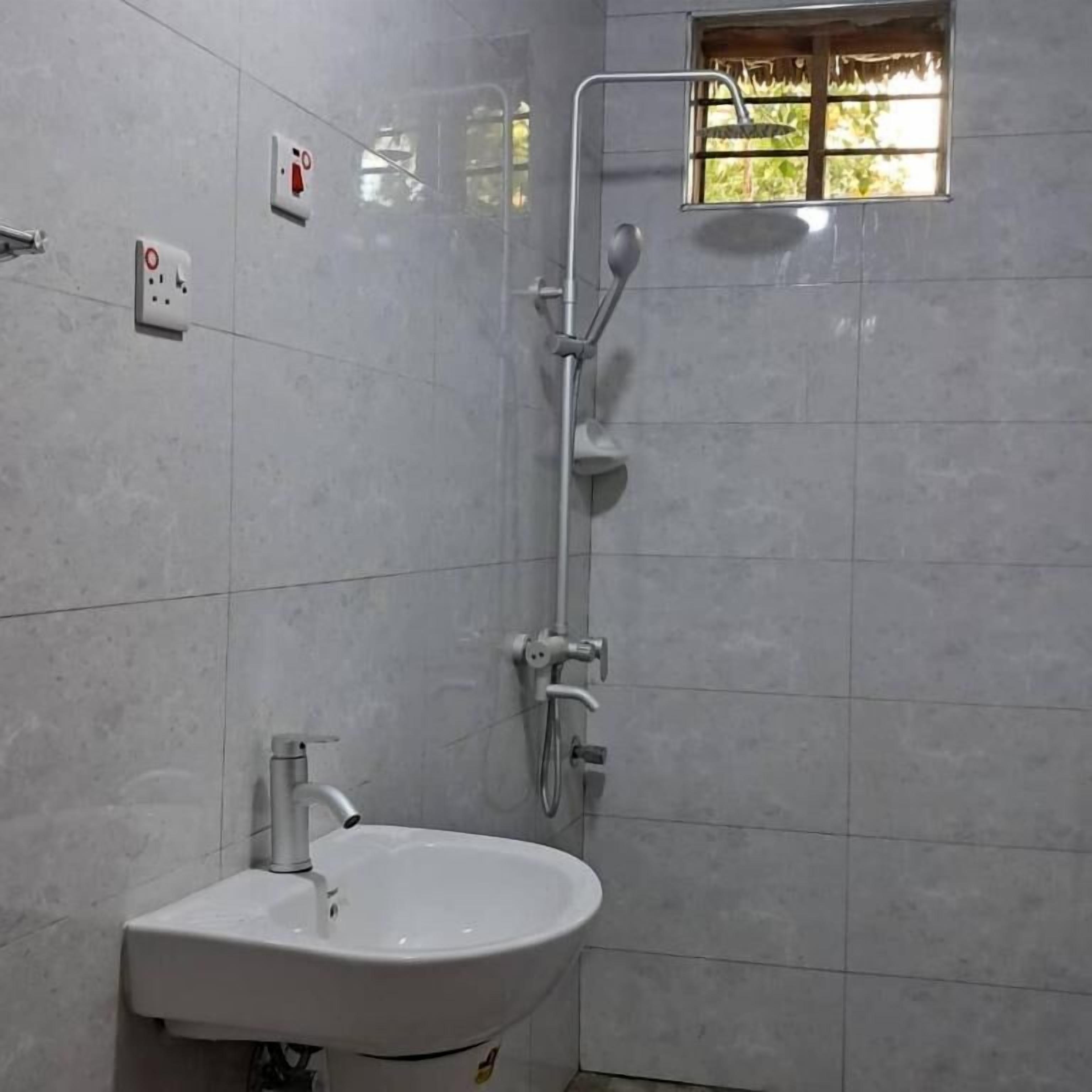 A bathroom with a white sink, a shower, and a window with a view of greenery.