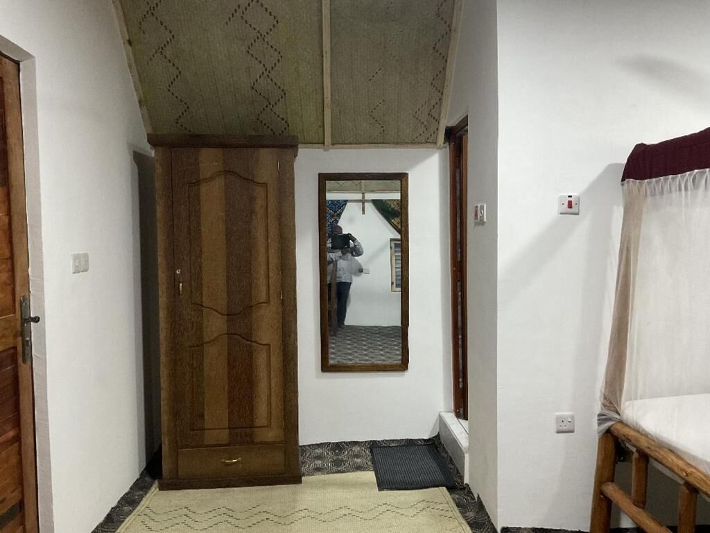 Un pasillo con una puerta de madera, un espejo y una cama con colcha blanca.