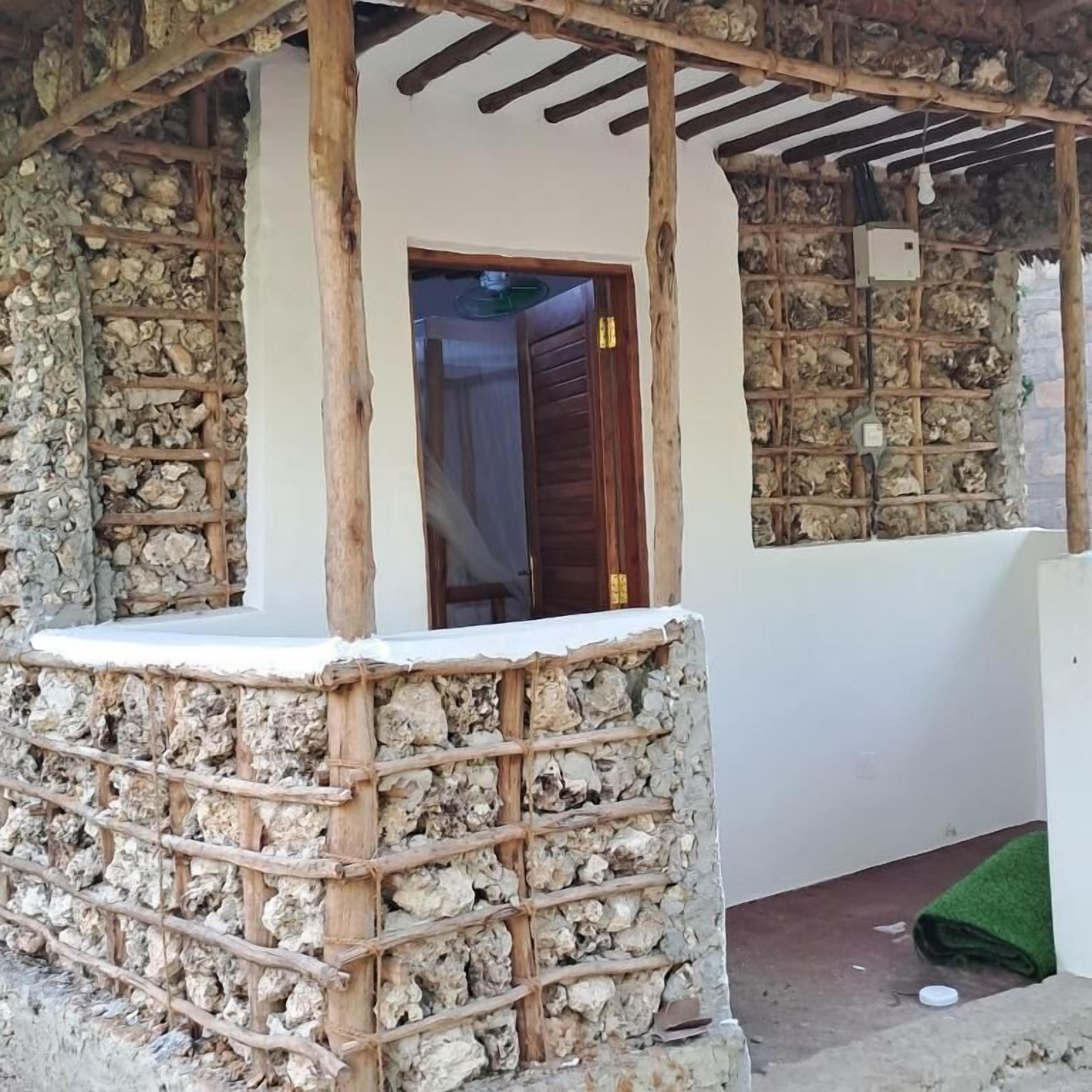 Un mur de pierres apparentes, avec une porte en bois et une petite construction en bois surmontée d’un toit.