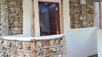 Un mur de pierres apparentes, avec une porte en bois et une petite construction en bois surmontée d’un toit.
