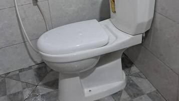 A white toilet with a bidet attachment in a tiled bathroom.