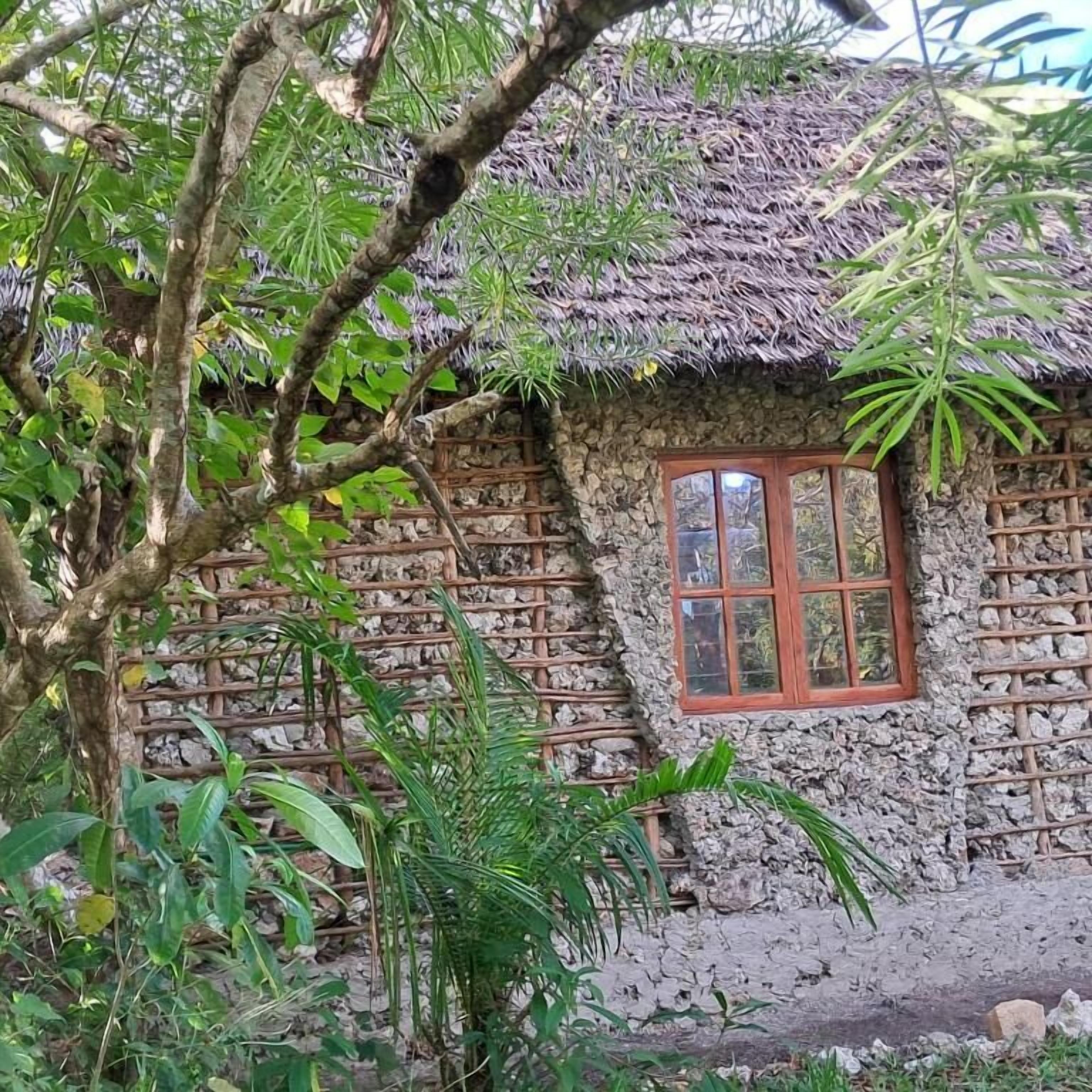 A rustic building with a thatched roof, a window with wooden shutters, and a stone wall.