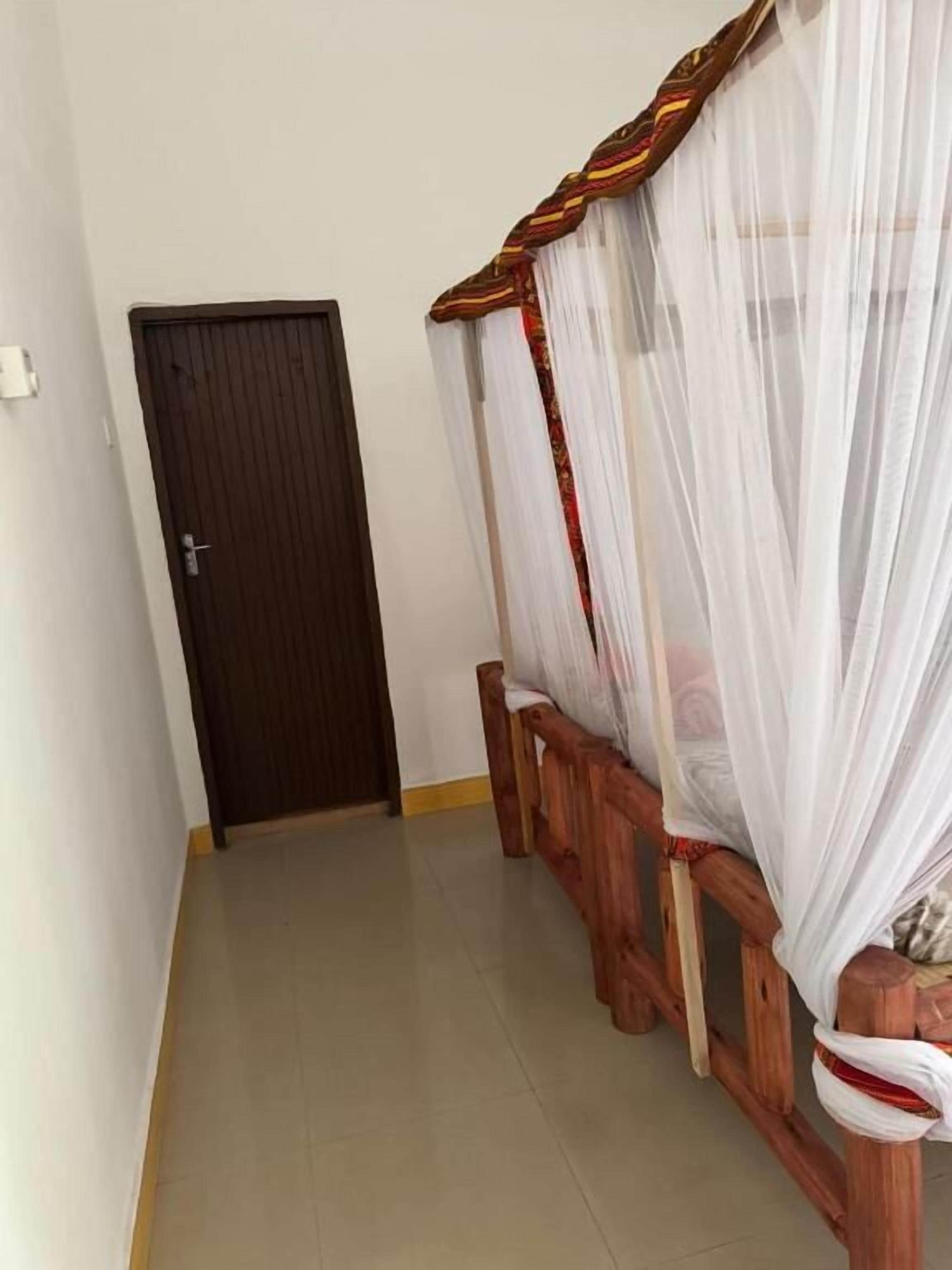 A room with a wooden bed with a canopy, a door, and a tiled floor.