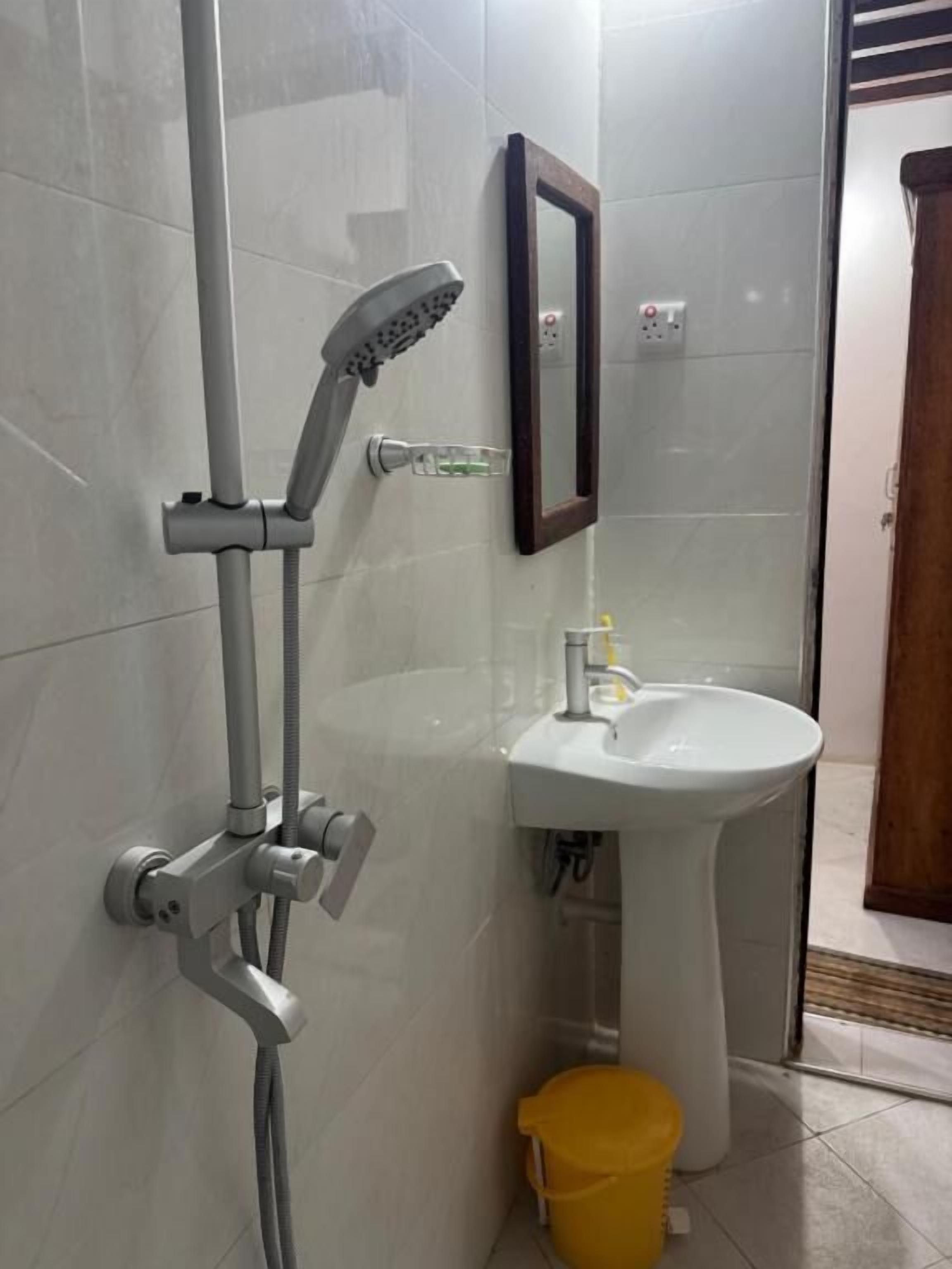 Un baño con ducha, lavabo y un cubo amarillo.