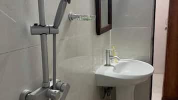 Un baño con ducha, lavabo y un cubo amarillo.