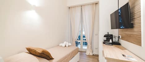 Una habitación de hotel con cama, escritorio con cafetera, televisión y ventana con cortinas.