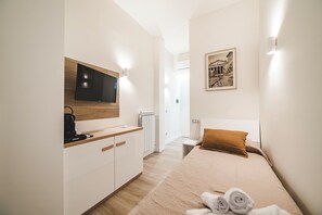 Ein modernes Hotelzimmer mit Bett, Schreibtisch, Flachbildfernseher, Heizkörper und einem gerahmten Bild an der Wand.