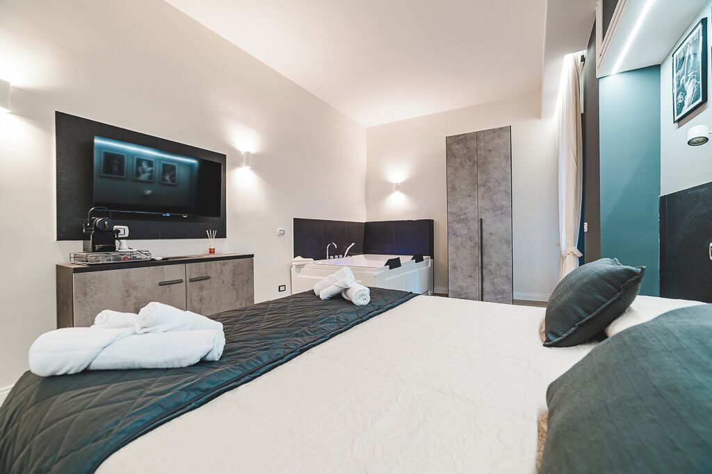 Una camera d'albergo moderna con un grande letto, una TV a schermo piatto montata a parete, una vasca da bagno e un angolo trucco con specchio.
