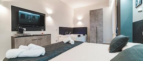 Une chambre d’hôtel moderne dotée d’un grand lit, d’un téléviseur à écran plat fixé au mur, d’une baignoire intégrée et d’une coiffeuse avec miroir.