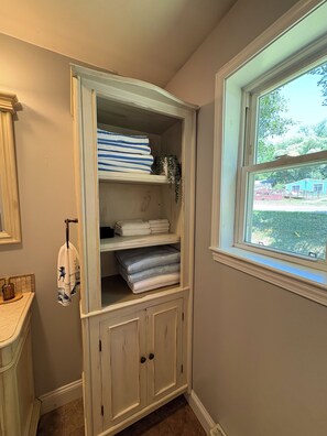 A bathroom with a built-in storage unit containing folded towels and a hanging towel.