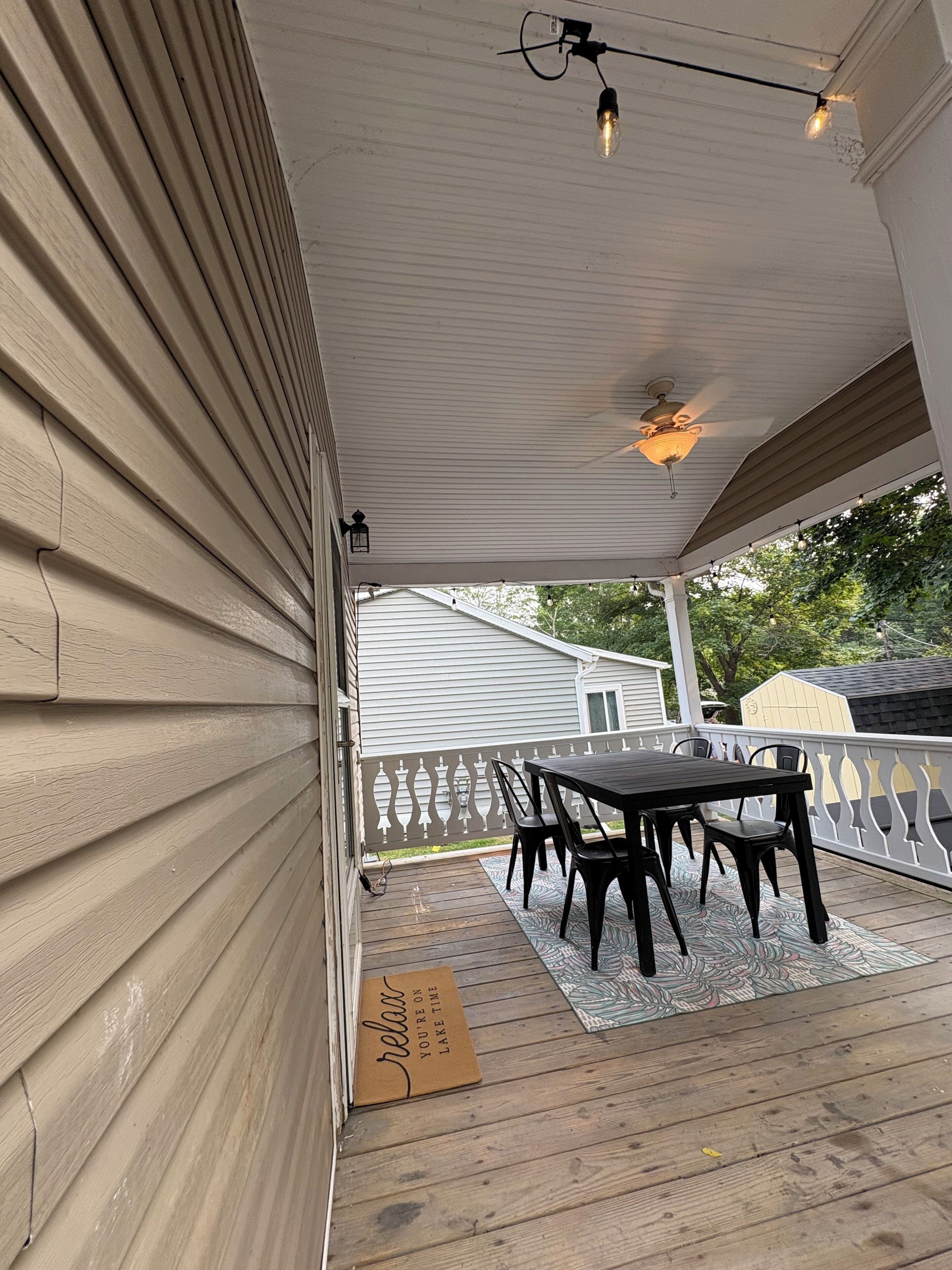 A covered patio with a table and chairs, a wooden deck, and a white railing.