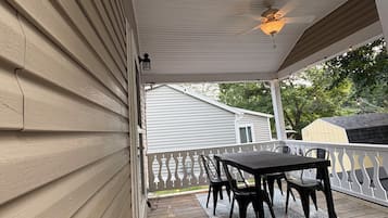 A covered patio with a table and chairs, a wooden deck, and a white railing.