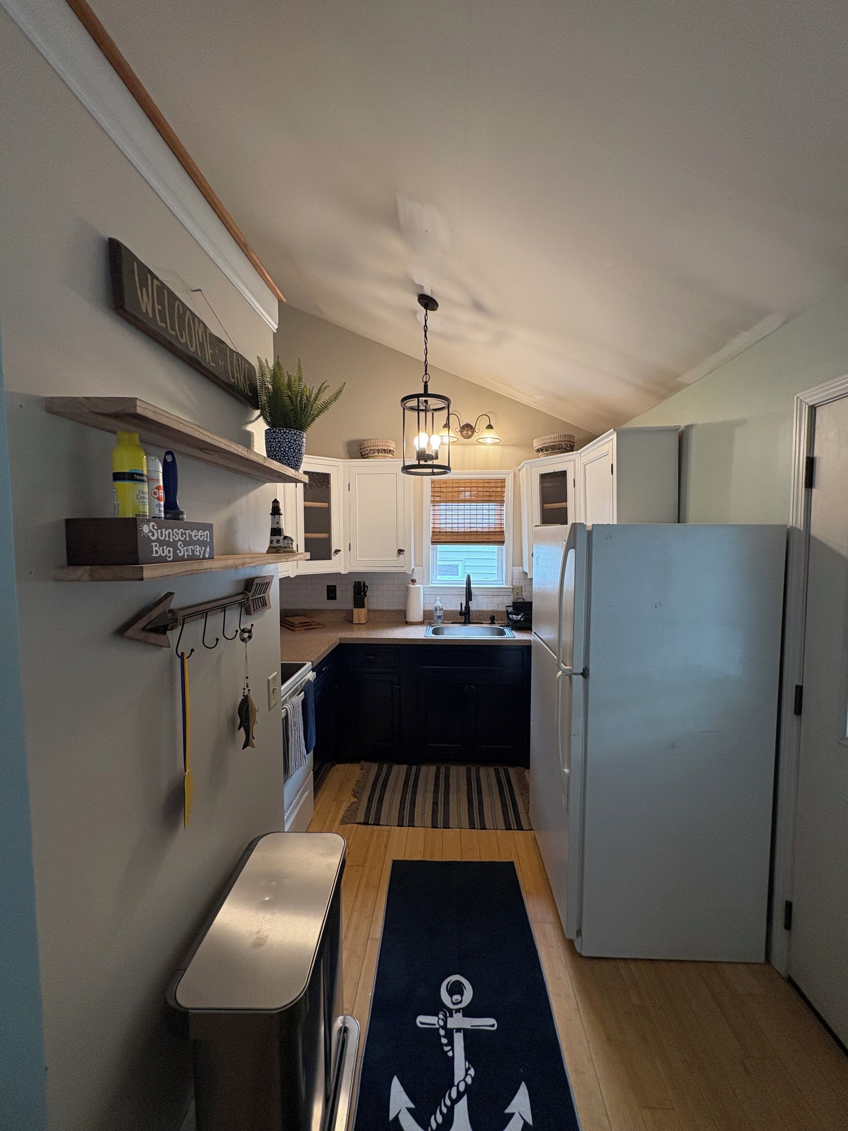 A compact kitchen with a built-in refrigerator, wooden cabinets, and a hanging light fixture.