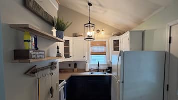 A compact kitchen with a built-in refrigerator, wooden cabinets, and a hanging light fixture.