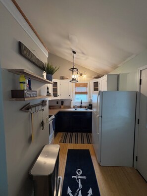 Een compacte keuken met een geïntegreerde koelkast, houten kastjes en een hanglamp.