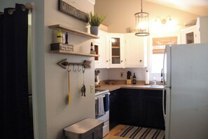 Una cocina con armarios blancos, encimera negra, refrigerador blanco y una planta colgante.