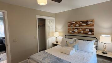 A hotel room with a bed, a ceiling fan, a wall-mounted fish decoration, and a door leading to another room.