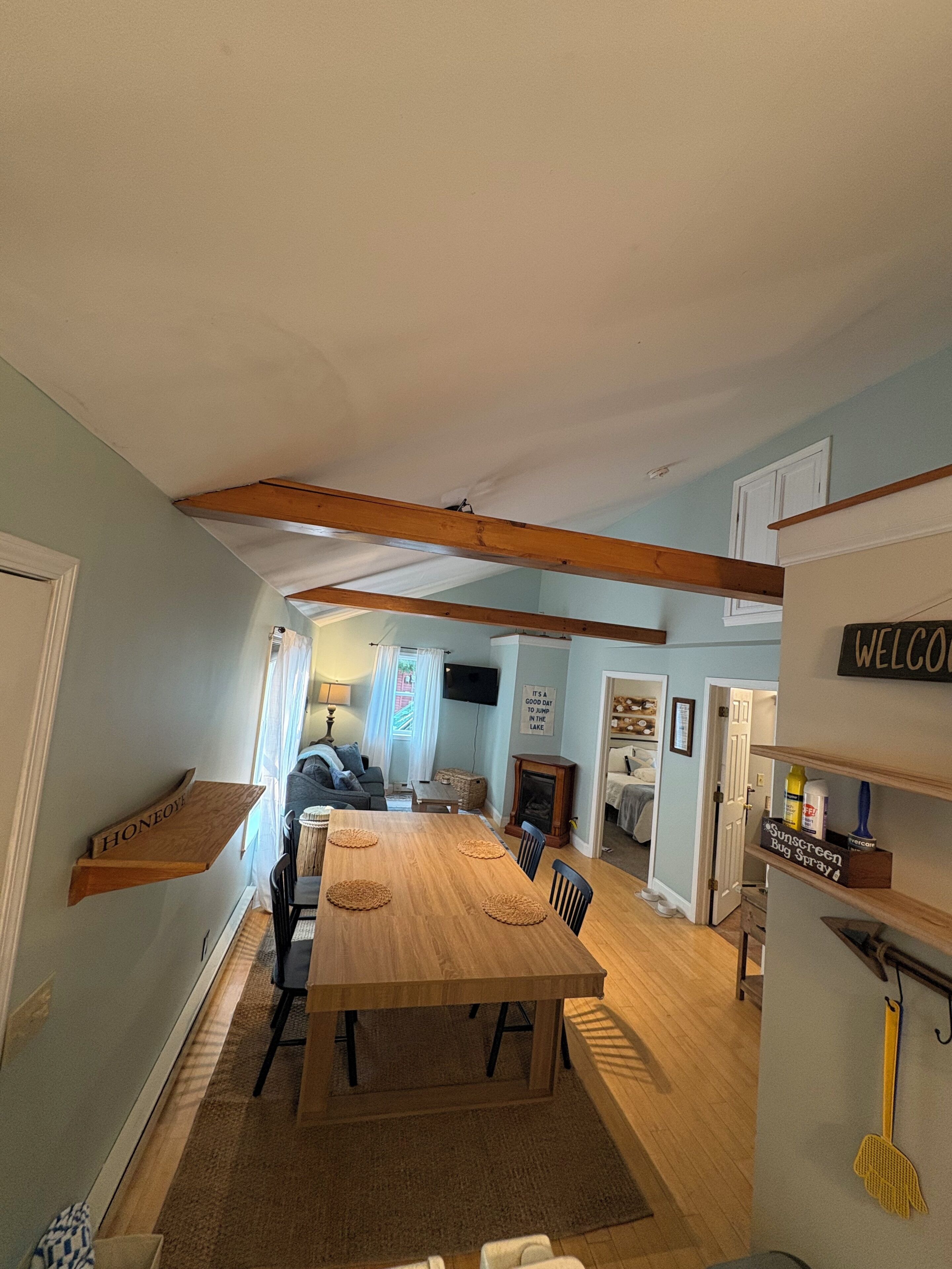 A dining area with a wooden table and chairs, a fireplace, and a 'WELCOME' sign.