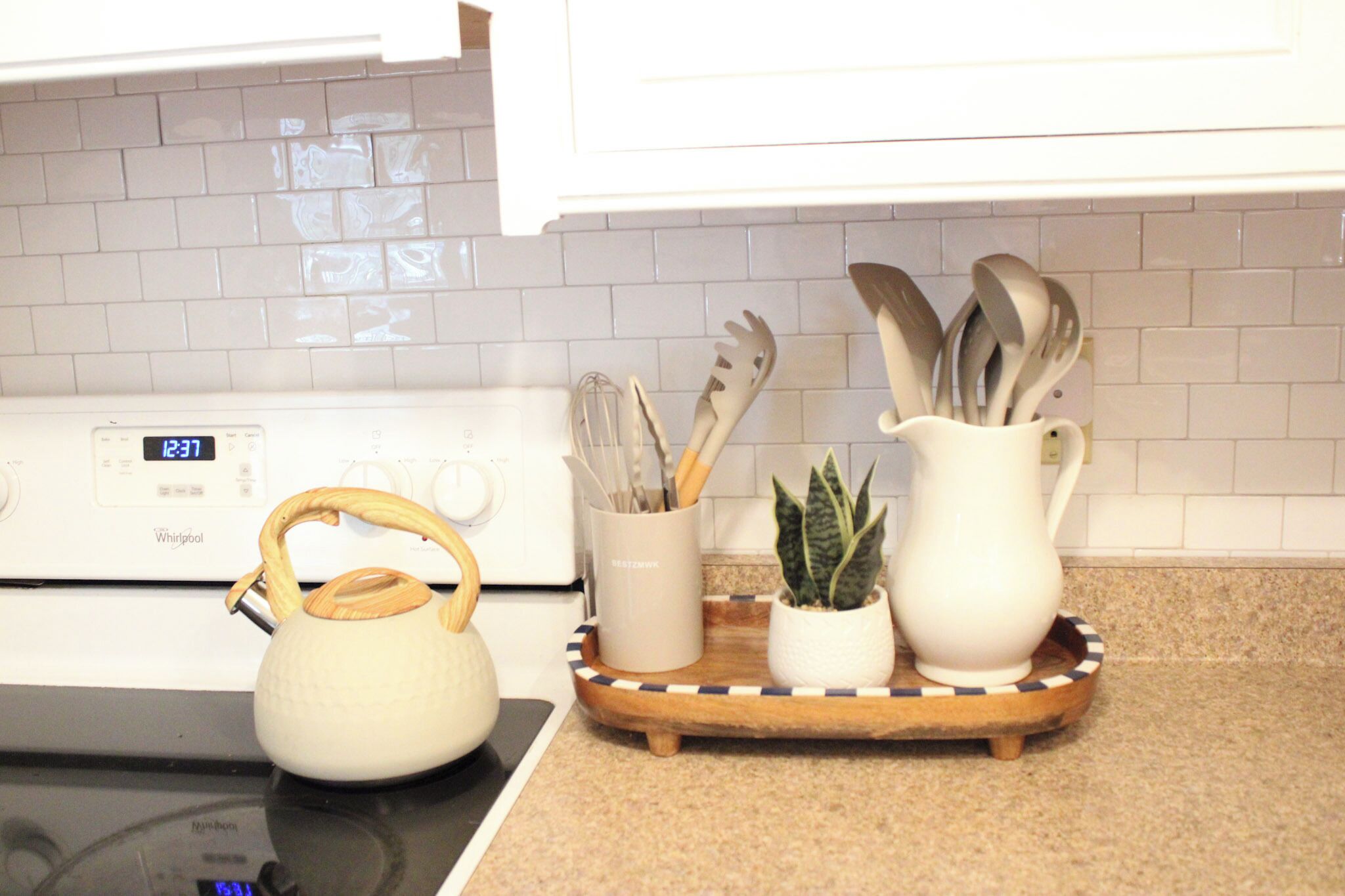 A kitchen with a white stove, a kettle, a tray with utensils, and a small plant.