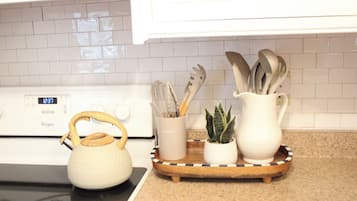 A kitchen with a white stove, a kettle, a tray with utensils, and a small plant.