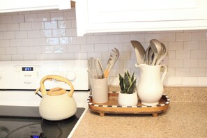 Cocina con estufa blanca, hervidor, bandeja con utensilios y una planta pequeña.