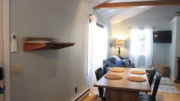 Un coin repas comprenant une table en bois, quatre chaises et une étagère fixée au mur, sur laquelle est accroché un panneau.