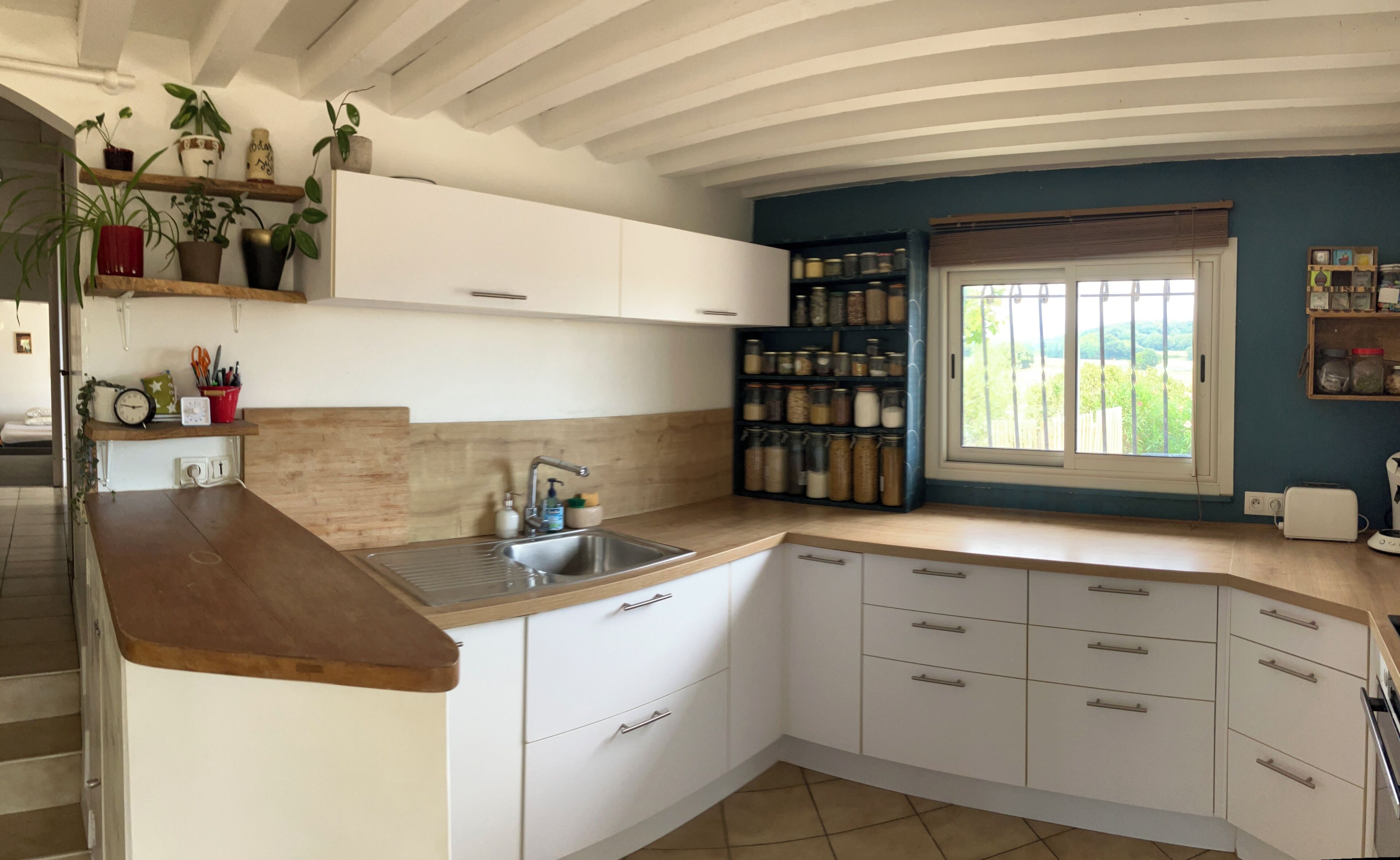 A kitchen with white cabinets, a wooden countertop, a sink, and a window with a view of greenery.