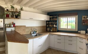 Una cocina con gabinetes blancos, encimera de madera, un lavabo y una ventana con vistas a zonas verdes.