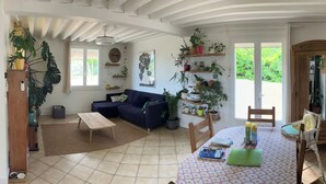 Ein Wohnzimmer mit einer Couch, einem Couchtisch und einem Essbereich mit Tisch und Stühlen. Mehrere Blumentöpfe und ein Deckenventilator sind vorhanden.