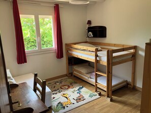 Una habitación infantil con una cama individual sobre otra, un escritorio, una silla, una alfombra con estampados de animales y una ventana con cortinas.