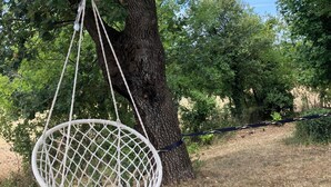 Ein weißer Makramee-Hängesessel, der an einem Baum in einer grünen Umgebung hängt.