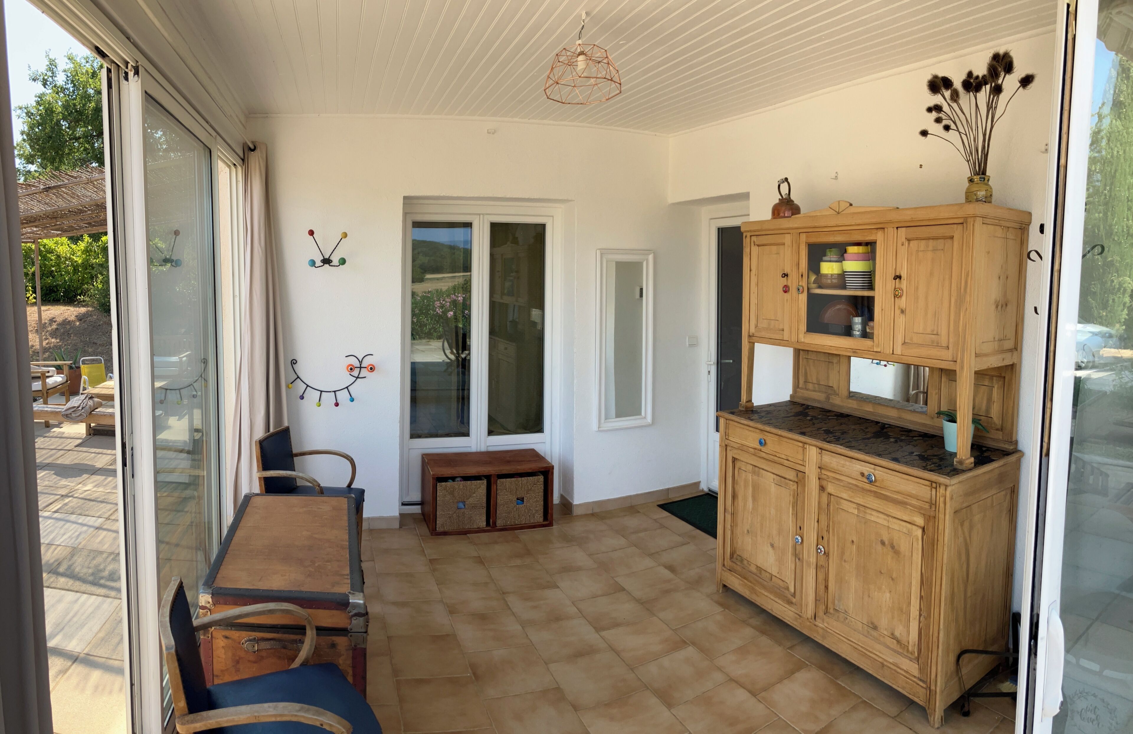 A room with a wooden cabinet, a table with chairs, and a sliding glass door leading to an outdoor area.
