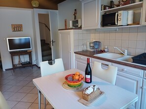 A kitchen with a dining table, a bottle of wine, a loaf of bread, and a bowl of fruit. - House in Banyuls-sur-Mer, on a quiet and beautiful pedestrian street 150 meters from the beach (Banyuls-sur-Mer)