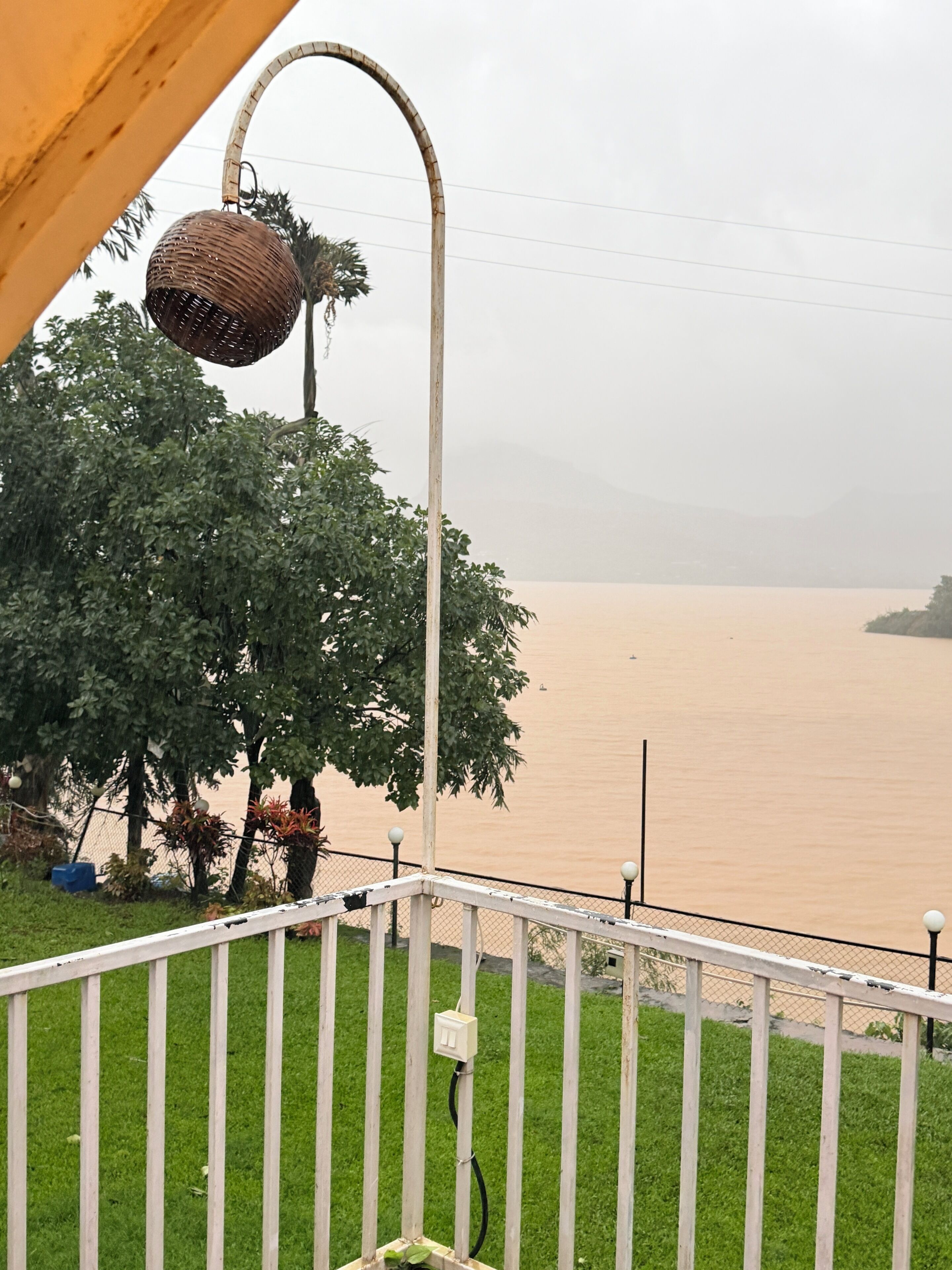 A view of a river with a fence in the foreground and a lamp post with a basket hanging from it.