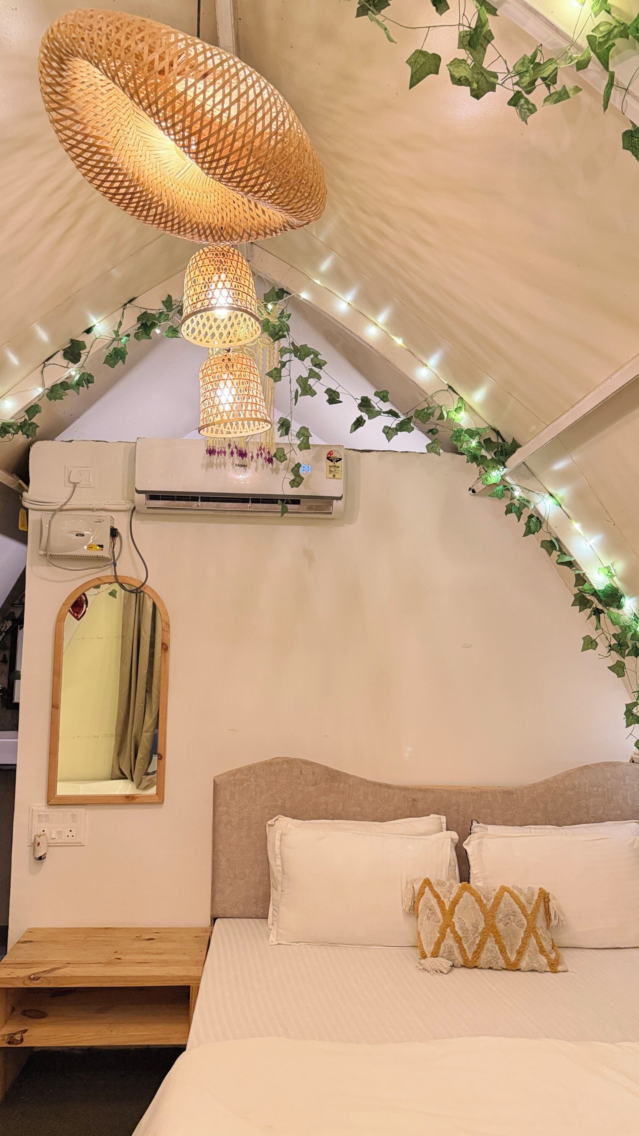 A tented room with a bed, a hanging lamp, an air conditioning unit, a mirror, and ivy decorations.