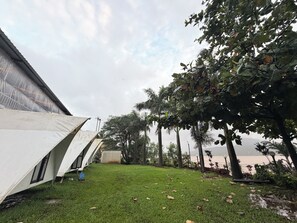 A grassy outdoor area with a white tent-like structure, trees, and a view of a body of water.