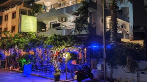 Ett hotell med en skylt, en uteservering med stolar och bord samt en väl upplyst entré.
