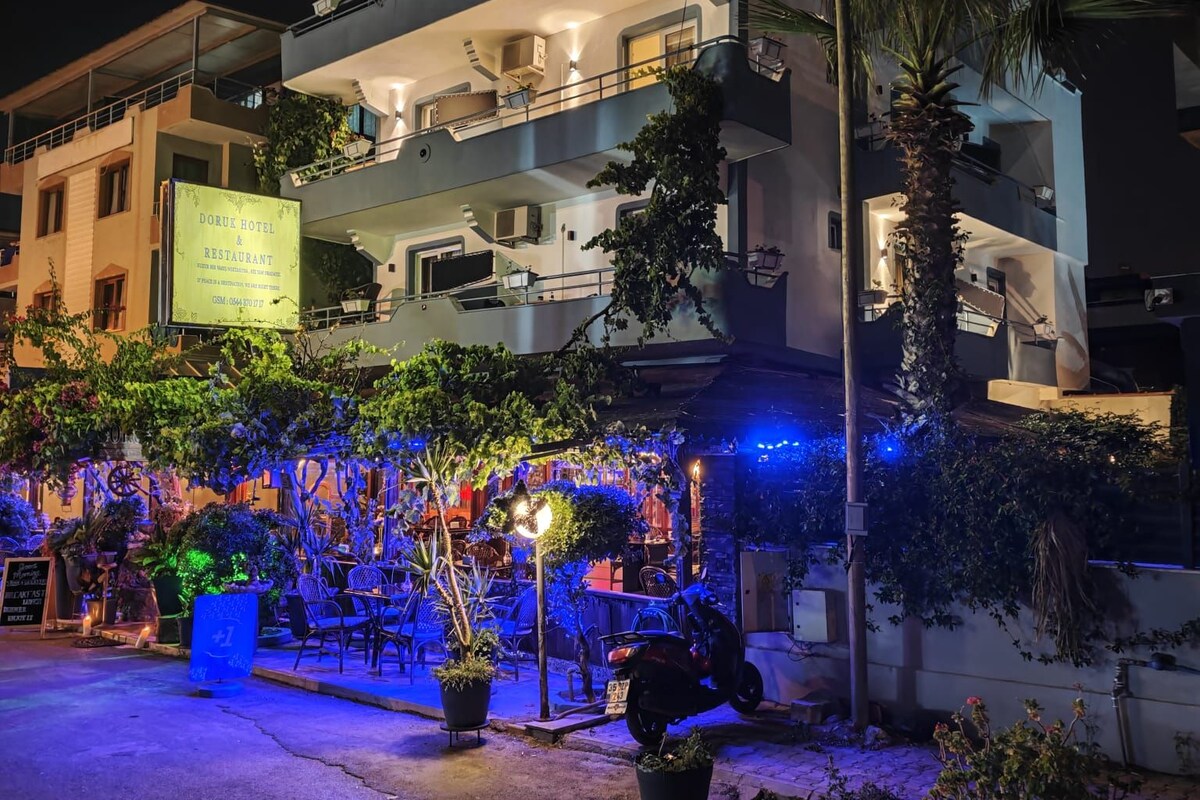A hotel with a signboard, outdoor seating area with chairs and tables, and a well-lit entrance.
