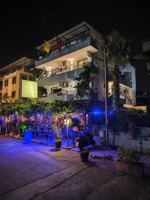 A hotel with a signboard, outdoor seating area with chairs and tables, and a well-lit entrance.