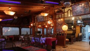 En restauranginteriör med synliga träbjälkar, bord med röda dukar och hängande discobollar.