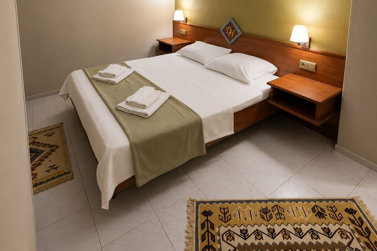 A hotel room with a bed, two bedside tables, a headboard, and two wall-mounted lamps.