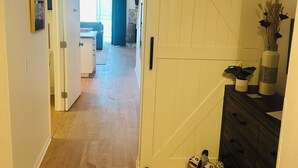 A hallway with a sliding barn-style door, wooden flooring, a dark-colored dresser with decorative items, and a small toy horse. - 2-bedroom 2-story renovated unit at The Cove Resort, park and walk downtown! (Lake Geneva)