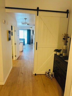 Un couloir doté d’une porte coulissante de style rustique, d’un plancher en bois, d’une commode de couleur sombre agrémentée d’objets décoratifs et d’un petit cheval en jouet.