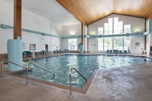 An indoor swimming pool with clear water, surrounded by lounge chairs and a wooden ceiling.
