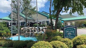 A hotel entrance with a sign reading "Welcome to The Cove of Lake Geneva," a landscaped garden with a water feature, and a building with a green roof. - 2-bedroom 2-story renovated unit at The Cove Resort, park and walk downtown! (Lake Geneva)