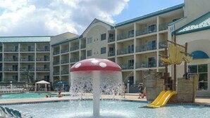 A hotel pool area with a water feature shaped like a mushroom, a slide, and a multi-story building with balconies. - 2-bedroom 2-story renovated unit at The Cove Resort, park and walk downtown! (Lake Geneva)