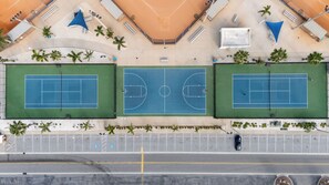 Luftaufnahme eines Tennisplatzkomplexes mit zwei Plätzen, Parkplätzen und umliegender Bepflanzung.